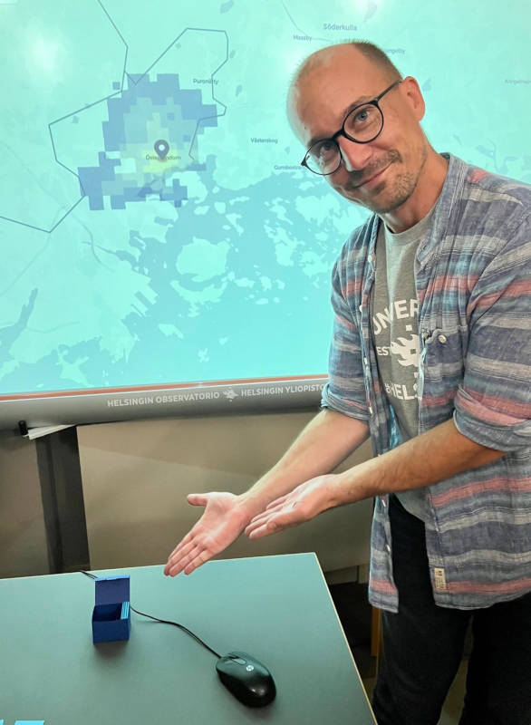 Christoph Fink in front of an interactive map screen, pointing at the playing cards used in one of the station