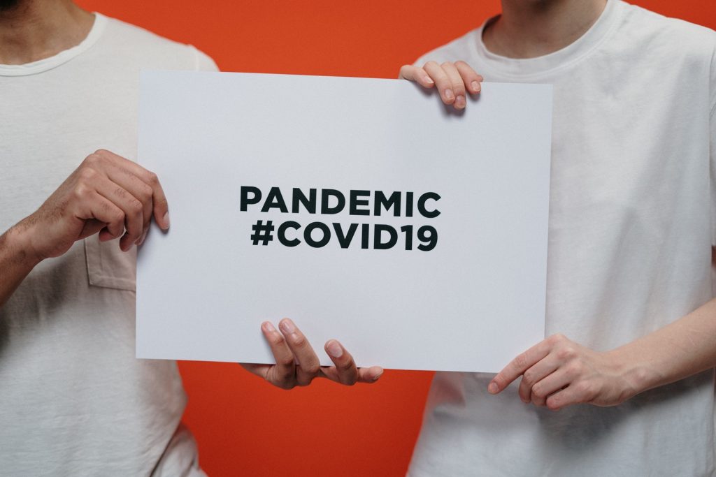 Two people holding white paper with the text pandemic #covid19