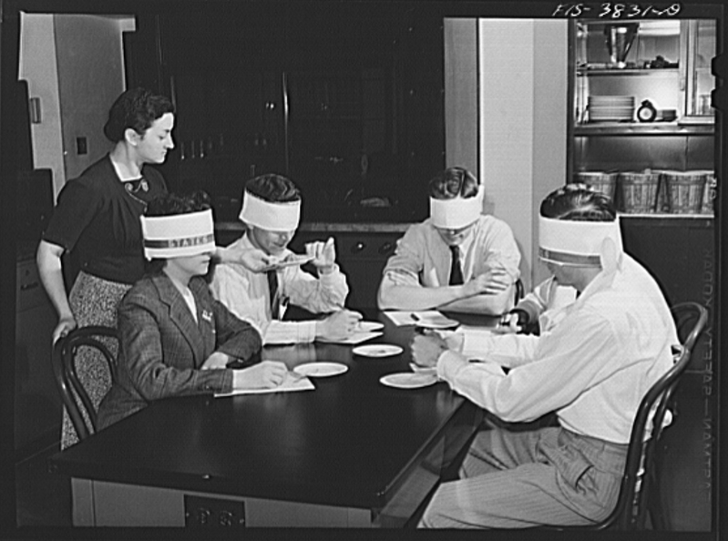 A black-and-white photo of a group of blindfolded people sitting at a table