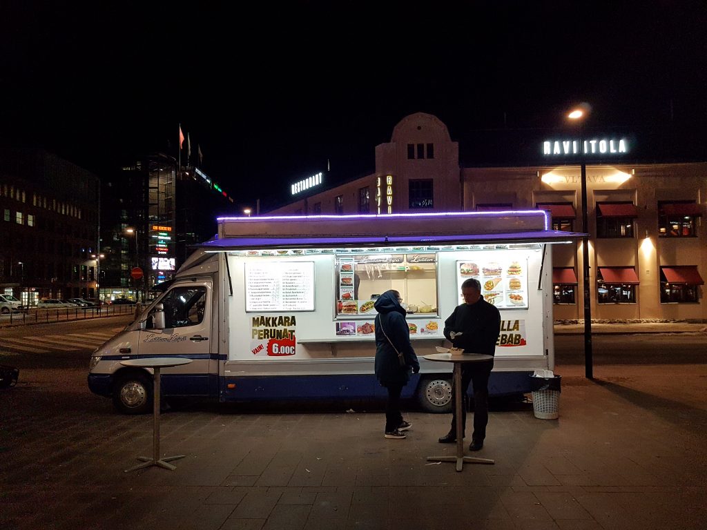 There are two people standing in front of a lit up food truck at night