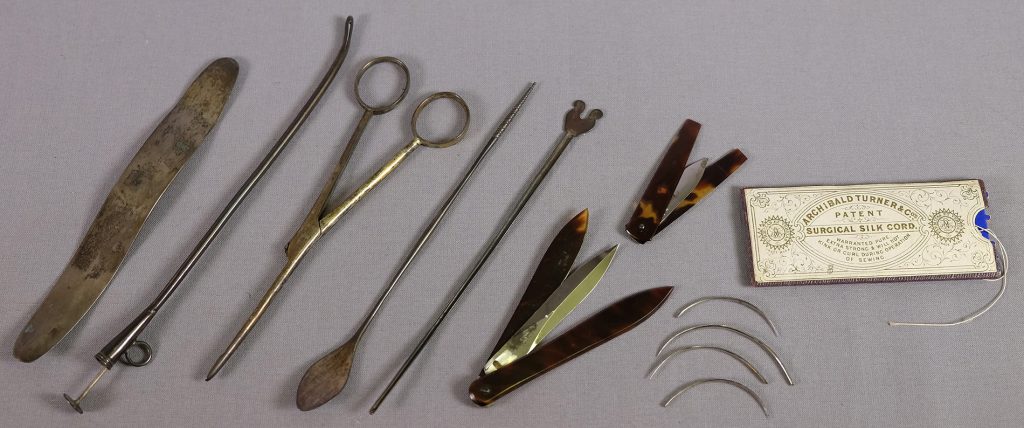 Sju stycken olika slags instrument, fyra nålar och en trådförpackning i papp ligger på rad.