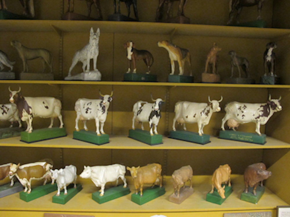 Små skulpturer av kor och hundar som står på gula hyllor.