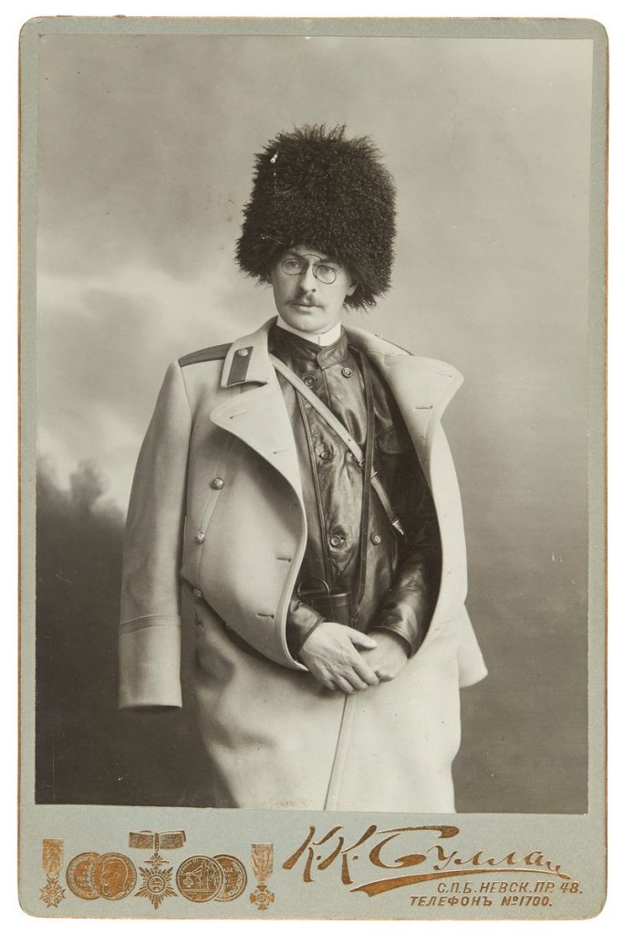 Ett svartvitt fotografi av en yngre Backmansson med en hög pälsmössa på huvudet och en ljus ytterrock över axlarna.