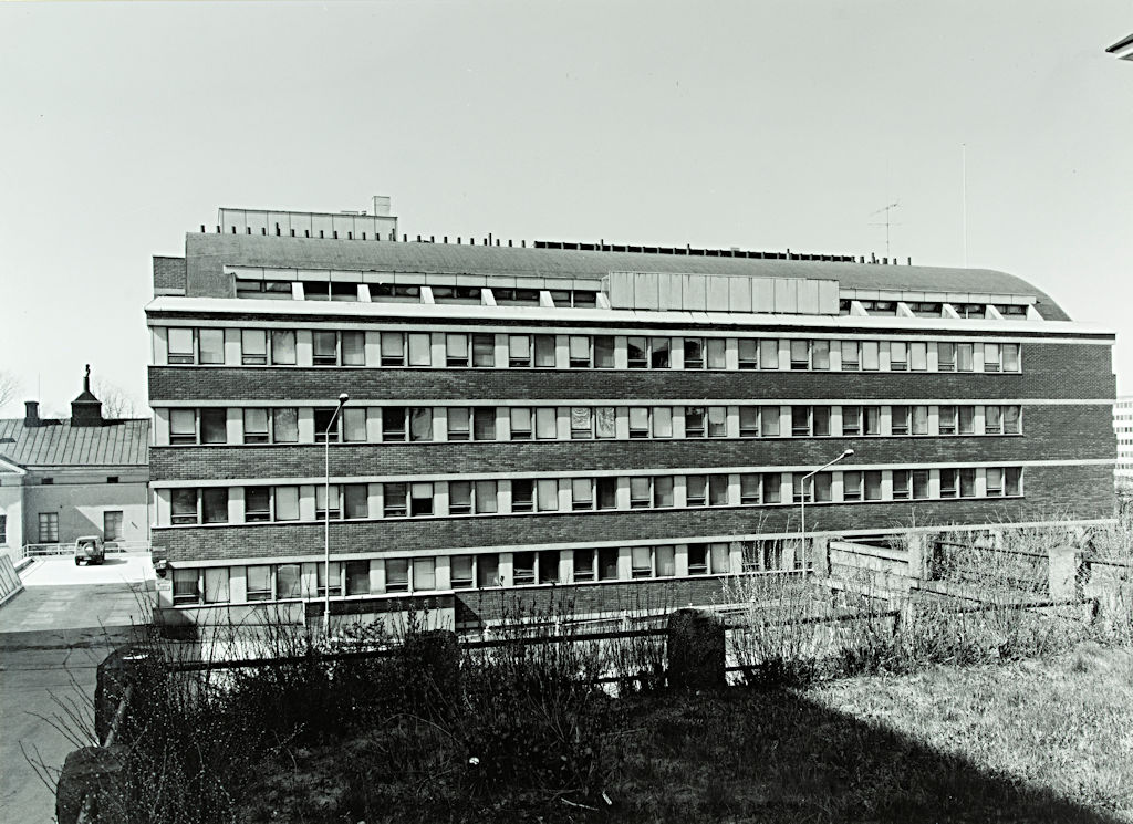 Det svartvita fotografiet föreställer ett av Helsingfors universitets fakultetsbyggnader. Huset har bandfönster. 