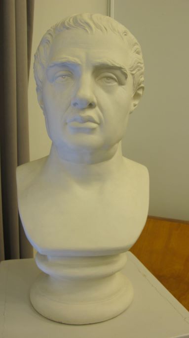 Ett vitt porträtt på en korthårig man. Skulpturen står på ett bord. Porträttet begränsas till mannens hals och övre delen av bröstet.