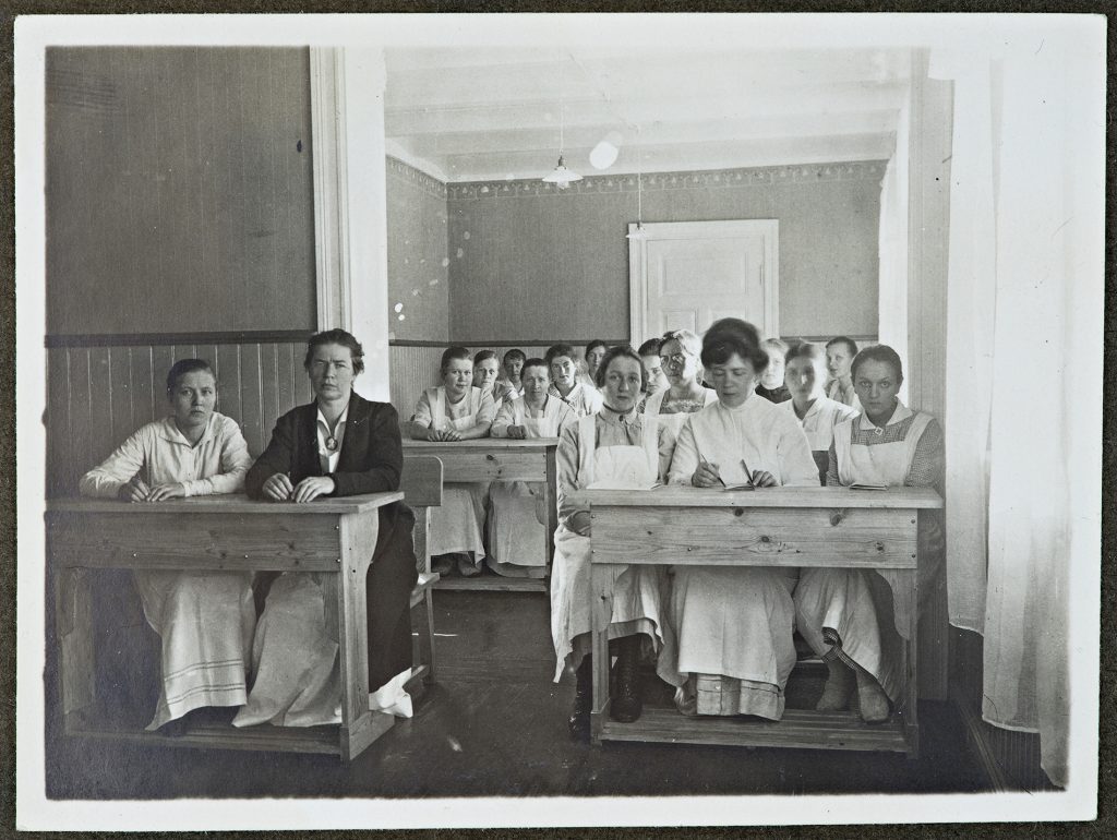 Gruppfoto på cirka 15 unga damer som sitter i parpulpeter. 