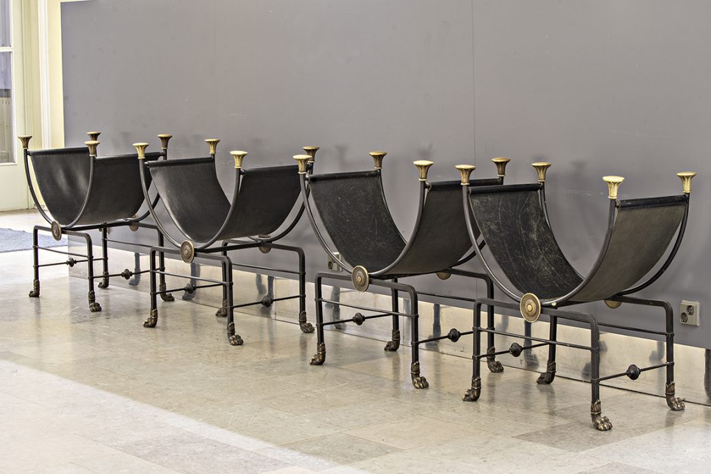 Fyra U-formade stolar som tillverkats av läder och smidesjärn i rad i en hall.