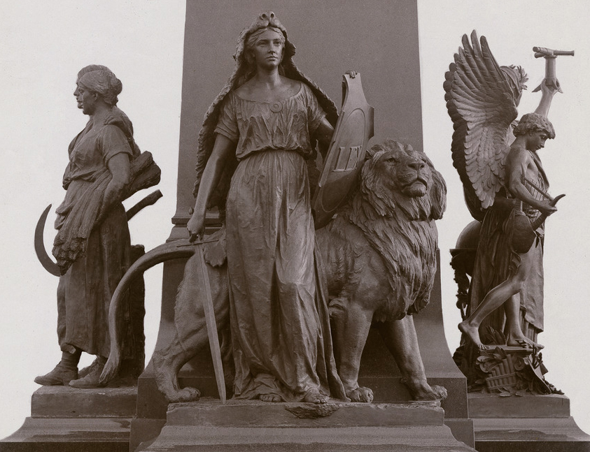 En skulptur som föreställer en kvinna och ett lejon. Kvinnan står framför lejonet. Hon har ett svärd och en sköld i händerna. 