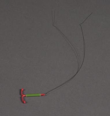 Ett litet plastföremål i form av bokstaven "T" med två långa trådar i spetsen.