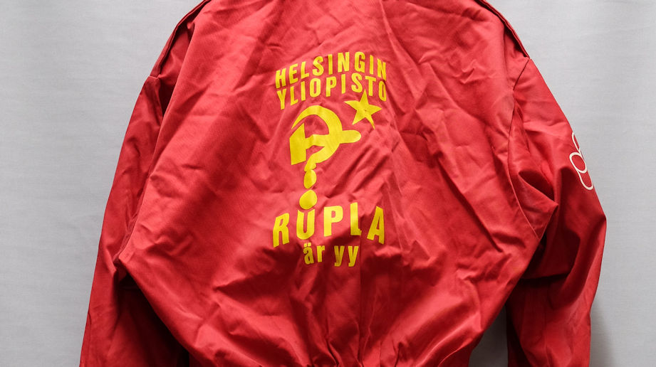 Symbols (a hammer and a sickle drawn in the form of a question mark) referring to the Soviet Union as well as text printed on a red, slightly crinkled piece of fabric.
