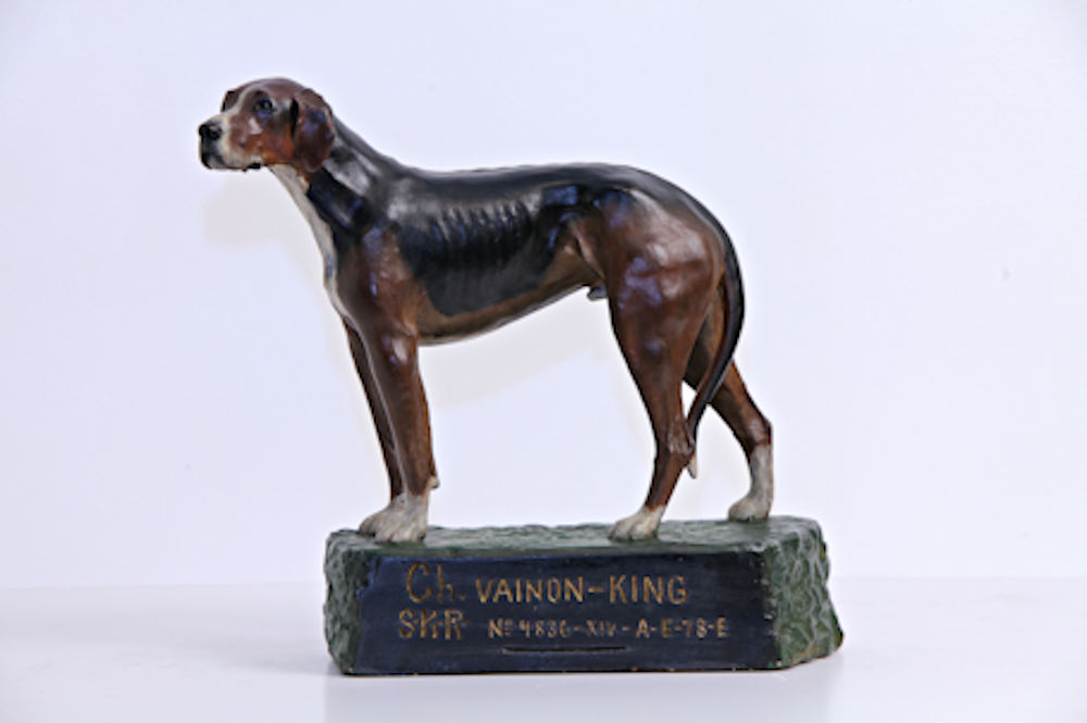 : A floppy-eared, black-, brown- and white-coloured dog stands on a green pedestal.