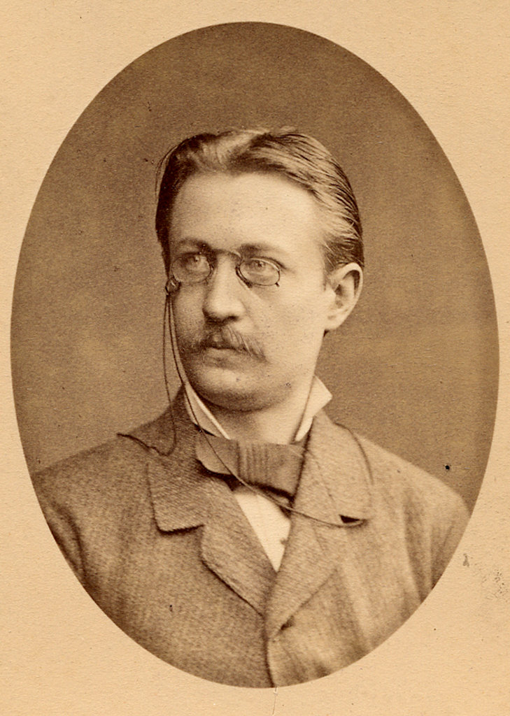 A moustachioed man wearing a suit and pince-nez. A bust in three-quarter profile.