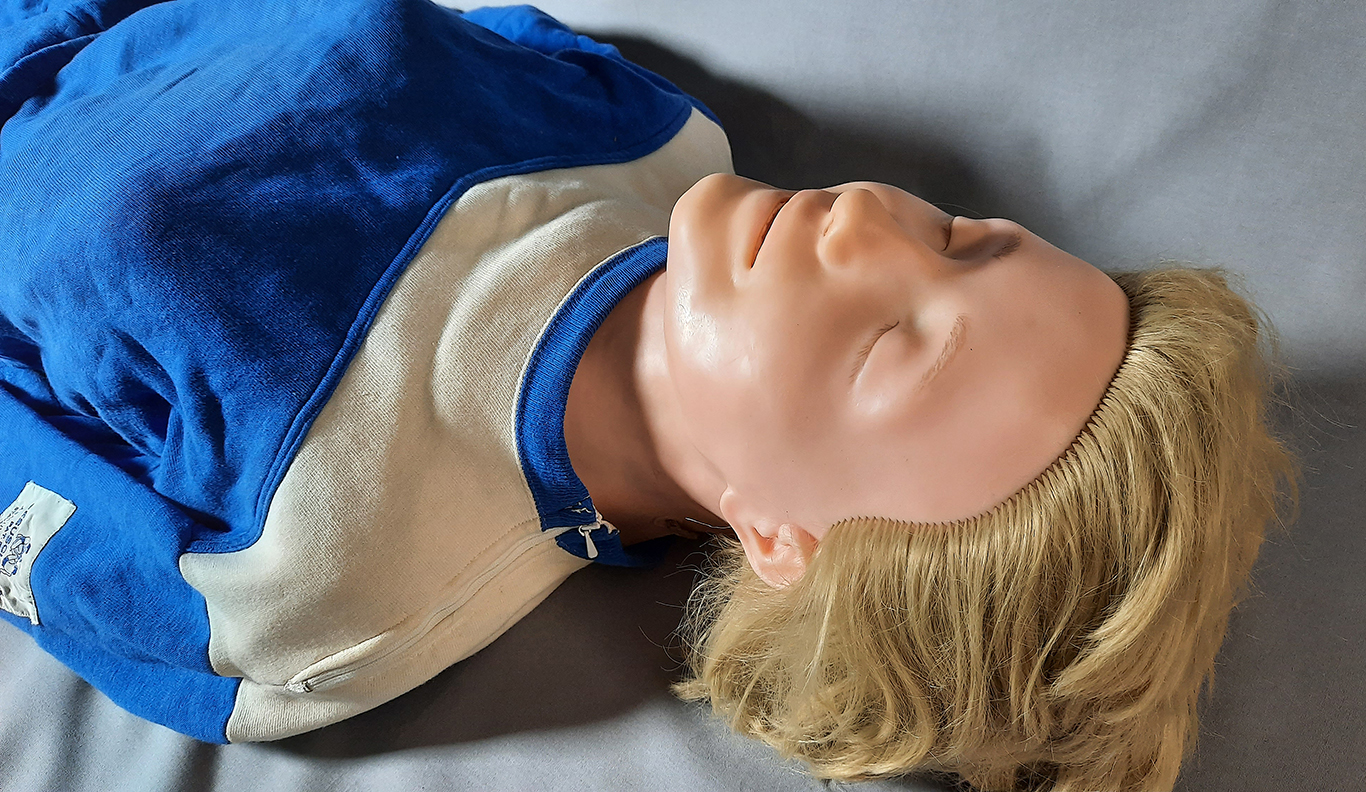 The upper body of Resusci Anne, wearing a tracksuit, viewed from the head of the manikin.