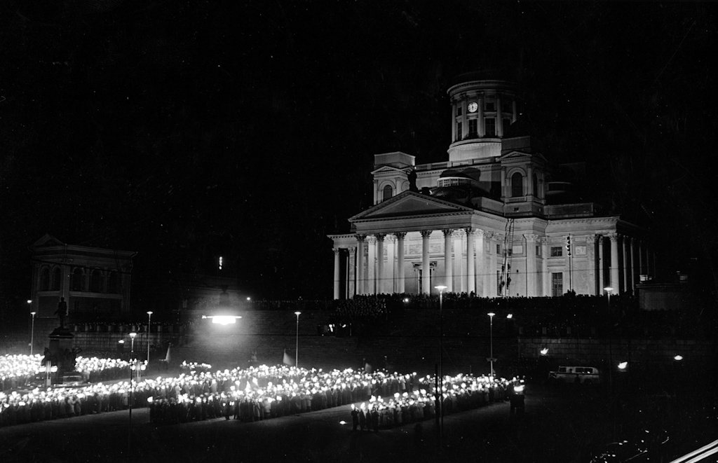 Rows of torches light up the darkness in the Senate Square. Some flags can also be spotted among them. Behind the crowd, on the right side of the picture, Helsinki Cathedral is clearly visible.