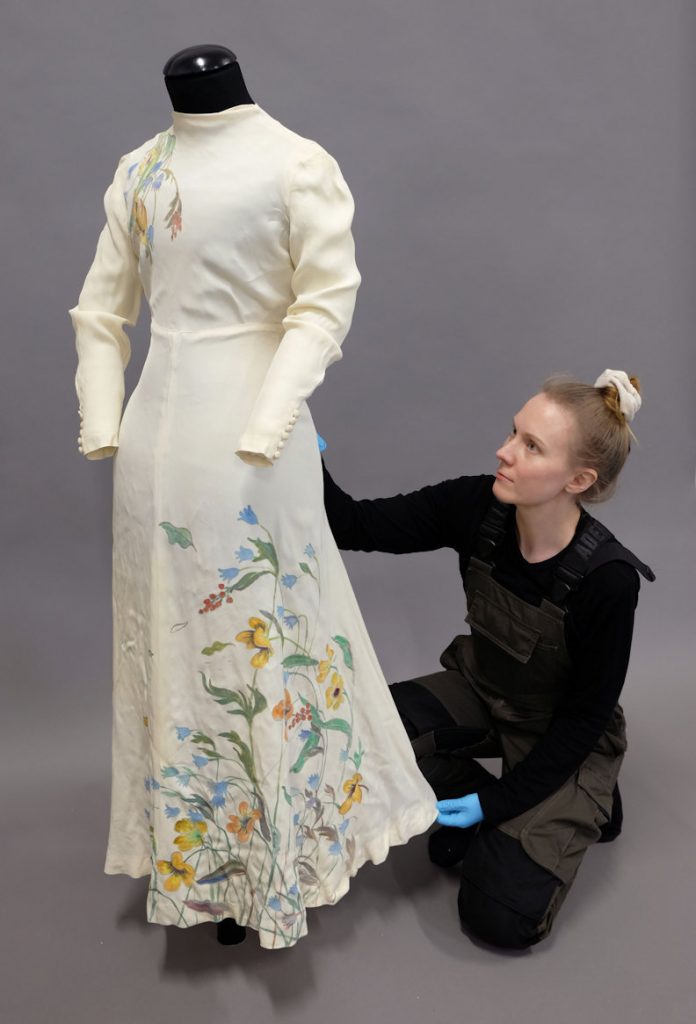 A person wearing dark work clothes and a mannequin wearing a light-coloured silk dress against a grey background.