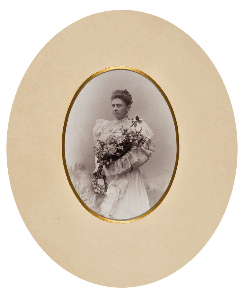 An oval photo of a young woman in a festive outfit holding a large bouquet of flowers.