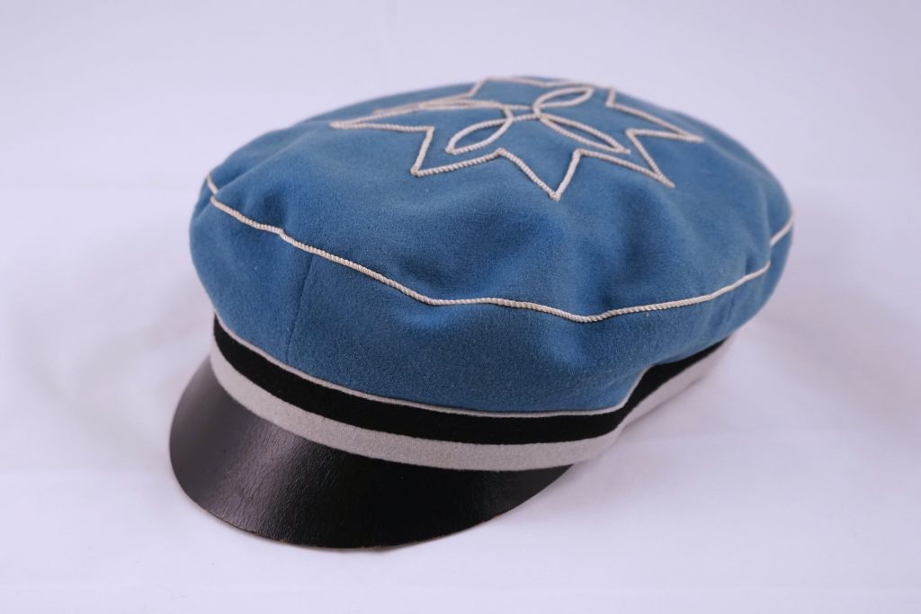 sinisest viltriidest valmistatud musta nokaga müts, mille alumises servas on must-valge triip ja lael valge rosett. 