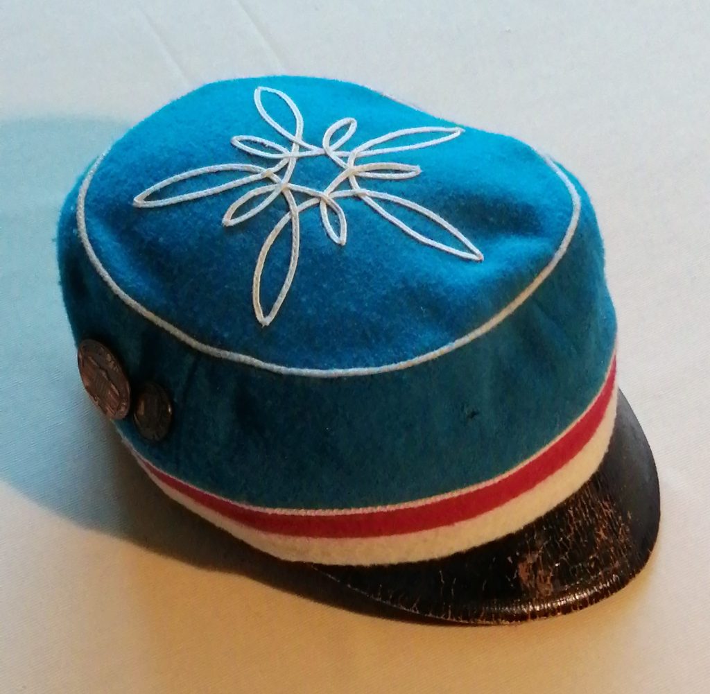 sinine musta nokaga müts, mille allservas on puna-valge triip ja lael valge rosett. 