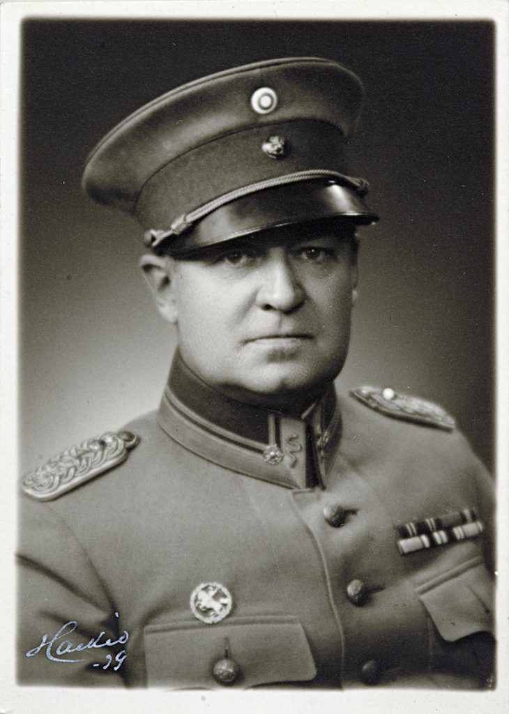A man in military uniform wearing a cap and looking straight into the camera.