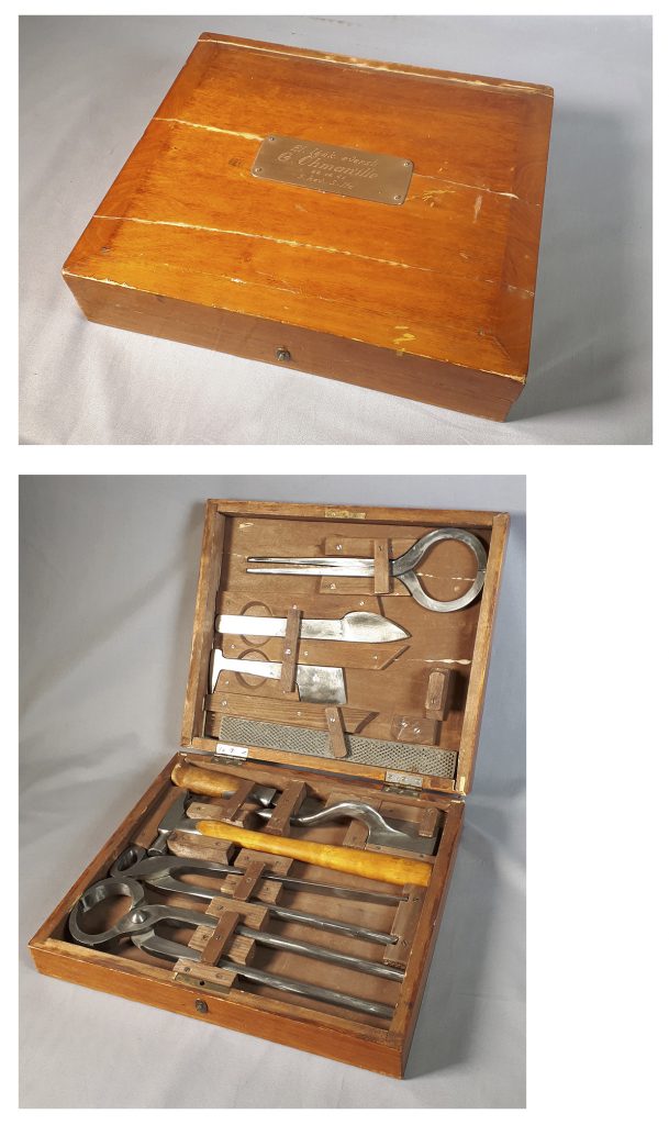 The first photo is of a flat wooden box with a metal plate on the lid bearing the names of the giver and recipient of the present. The second photo shows the box open, revealing farrier tools attached to the lid and bottom of the box with small wooden pegs.