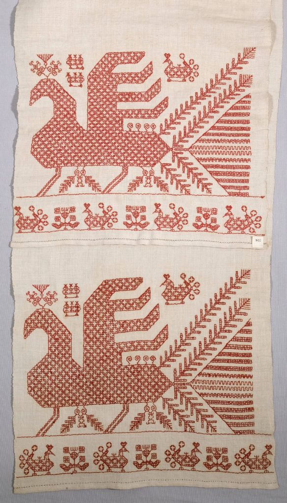 A long cloth photographed so that both ends are visible side by side. The embroidered figure represents a large bird, above and below which are a row of small birds.