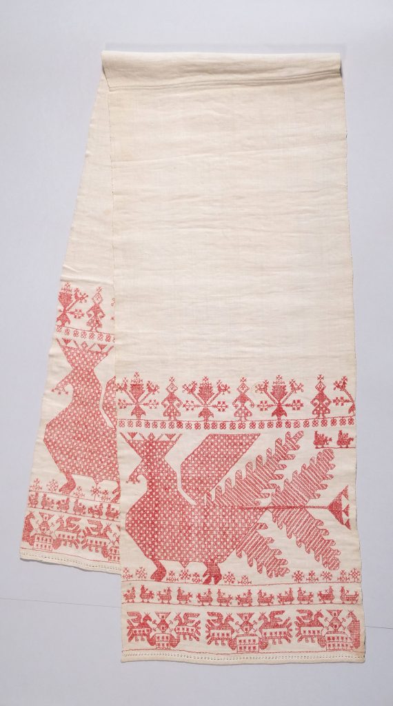 A long, narrow cloth folded in half in the middle so that both ends are visible side by side. Embroidered at the ends are large bird motifs, below which are a row of small birds and, still below, another row of birds in reverse order.