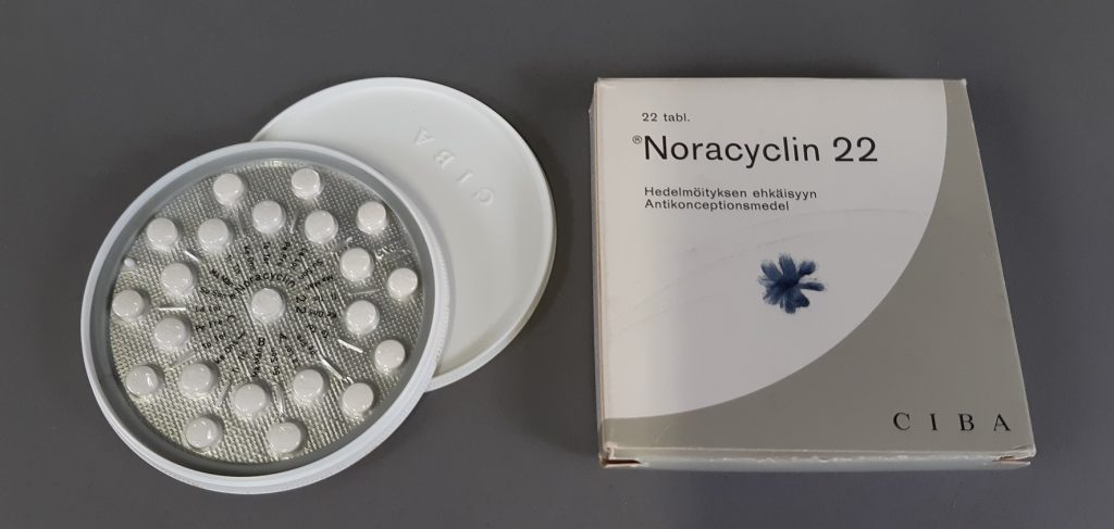 A carton with the words Noracyclin 22 and a round, white plastic container with white tablets in a round blister pack.