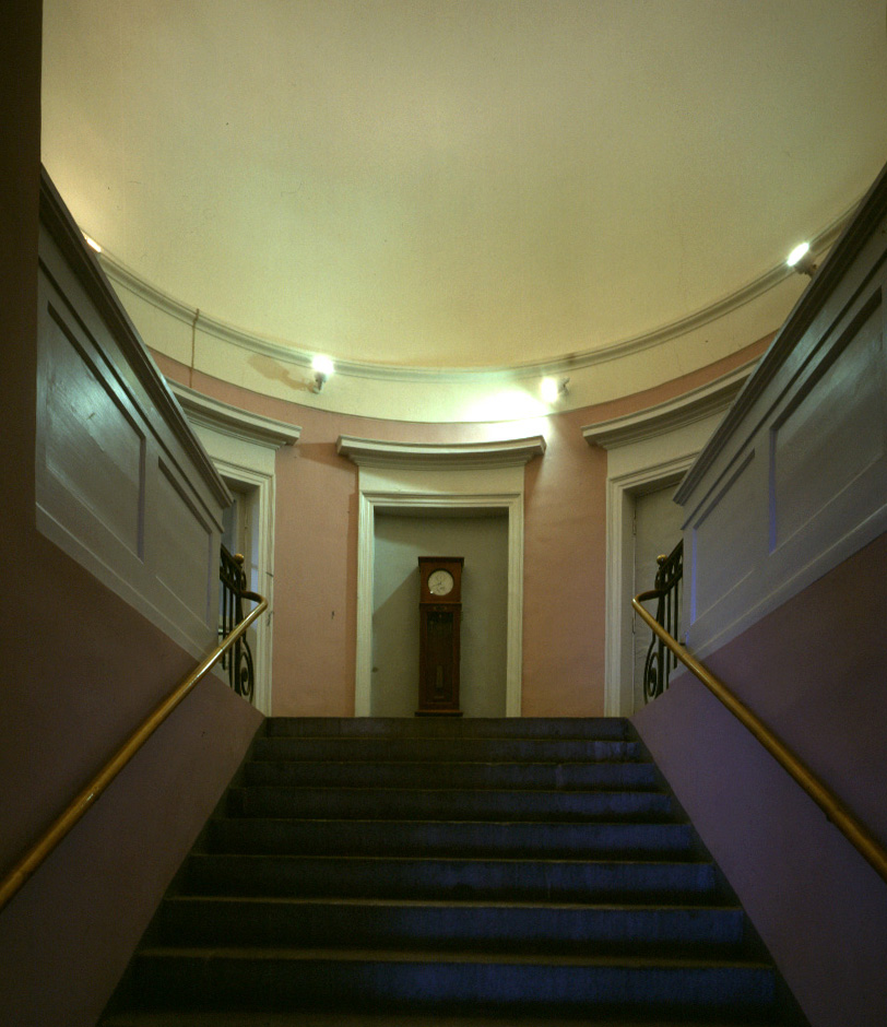 Aulatilassa on portaat ylätasanteelle, jossa näkyy kaappikello seinällä.