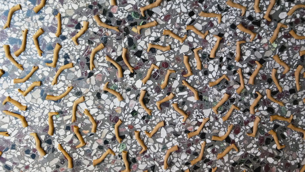 An artwork consisting of small clay limbs scattered over multi-colored floor