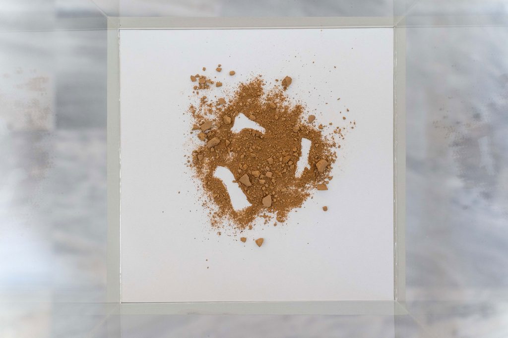 An artwork of traces of limbs within powdered brown clay on a white background