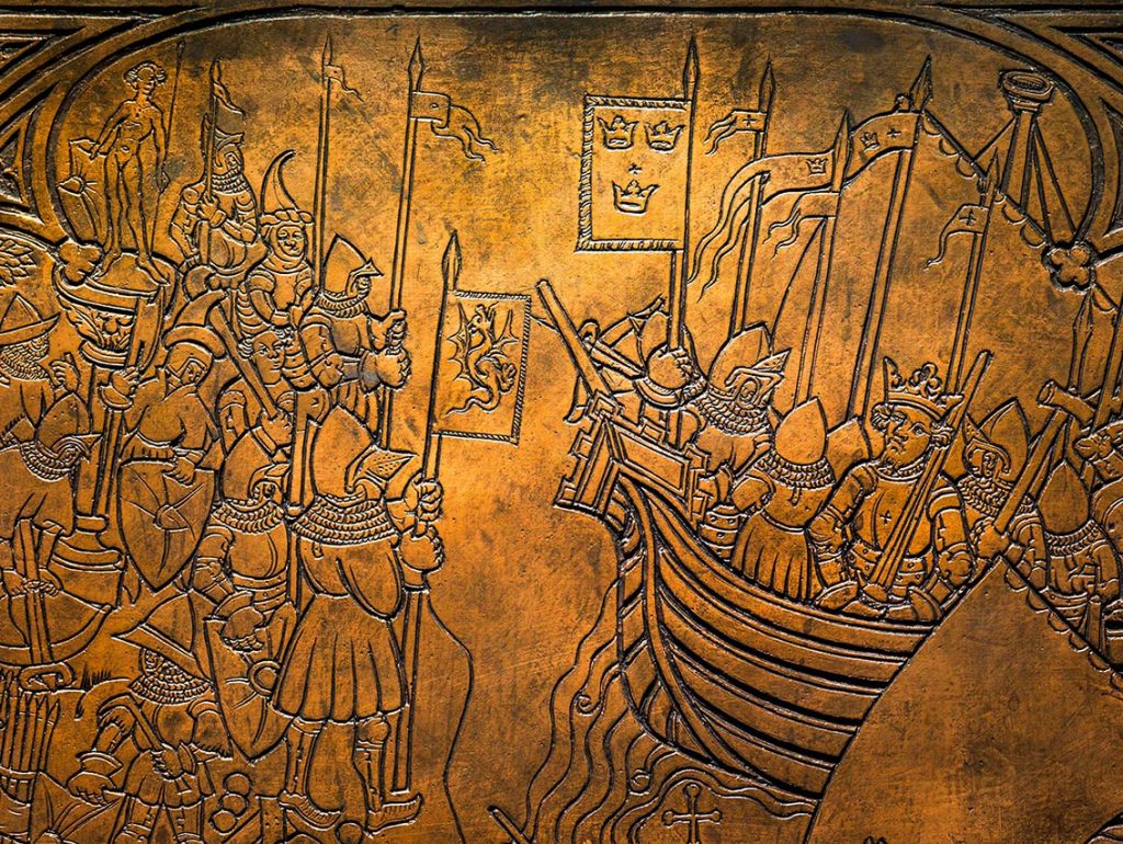 Lämpimän kuparinruskeaan messinkilevyyn on kaiverrettu ristiretkeläisten laiva purjeineen, lippuineen ja keihäineen, ja joka saapuu rantaan, missä on ihmisjoukko vastassa.