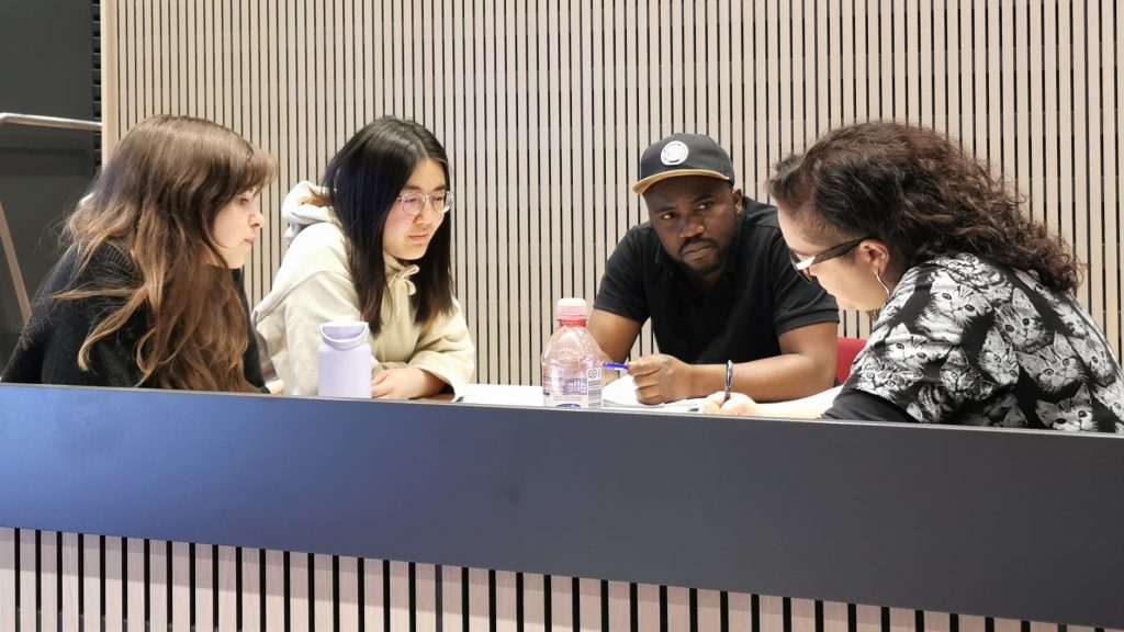 En grupp på fyra deltagare diskuterar vid ett bord och skriver ett gemensamt mentorskapsavtal.