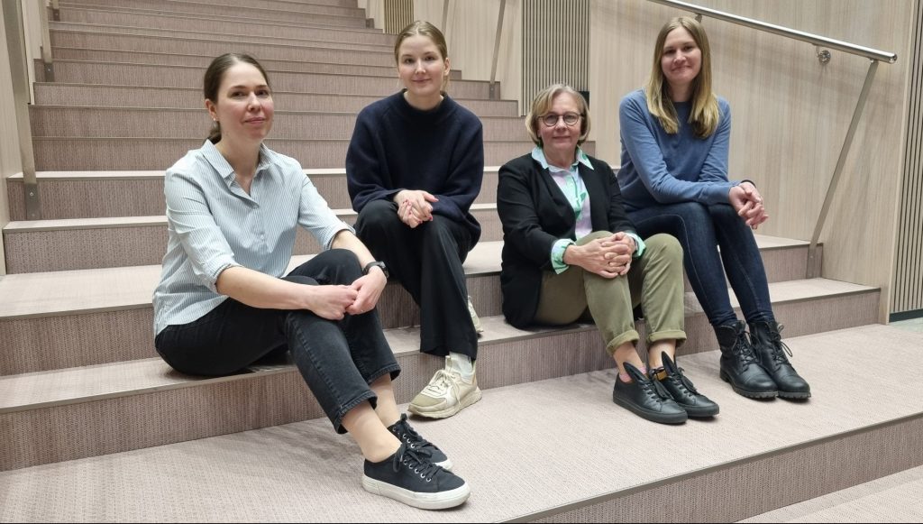 Anne Rahikka, Saara Hannula, Vilma Turunen, and Ellinoora Ekman sitting on the stairs of the lecture hall.
