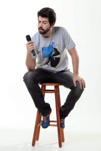 Comedian sitting on a stool.