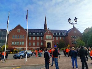 People in orange shirts gathered in front of a large brick building 