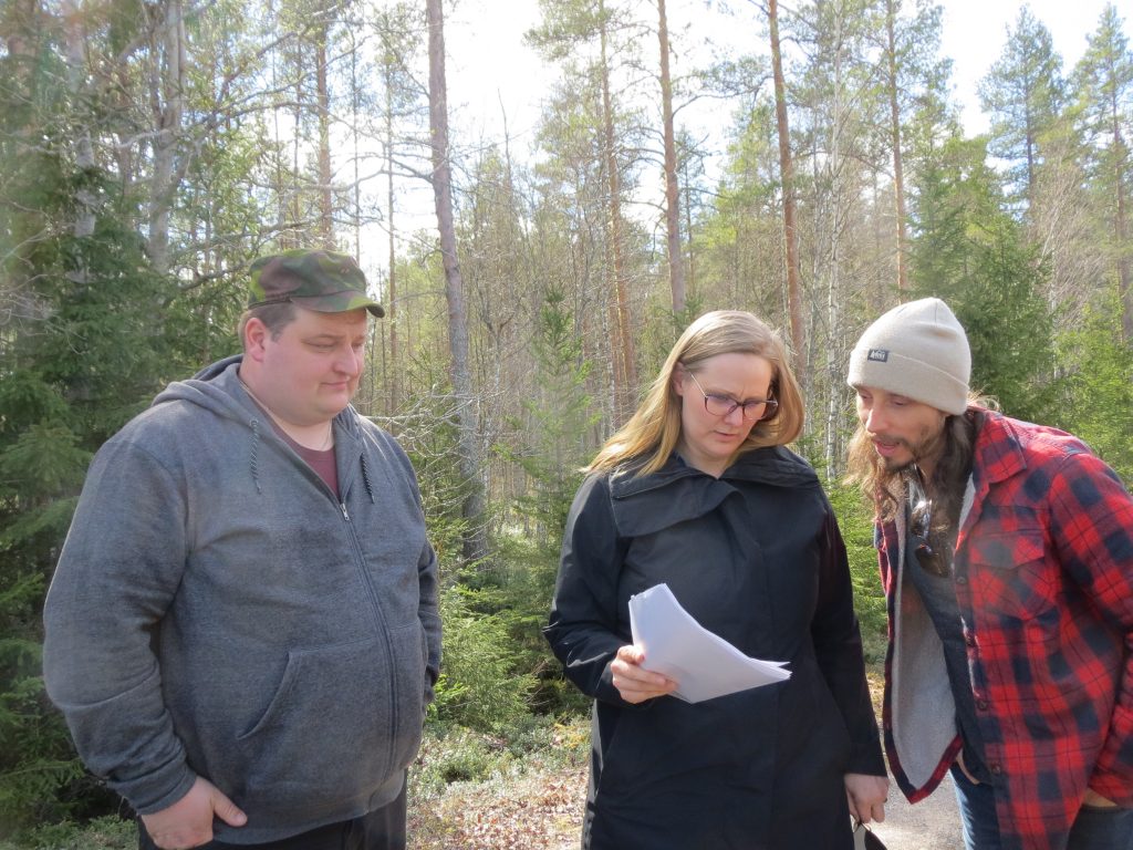 Three people looking at paper documents outside in the forest.