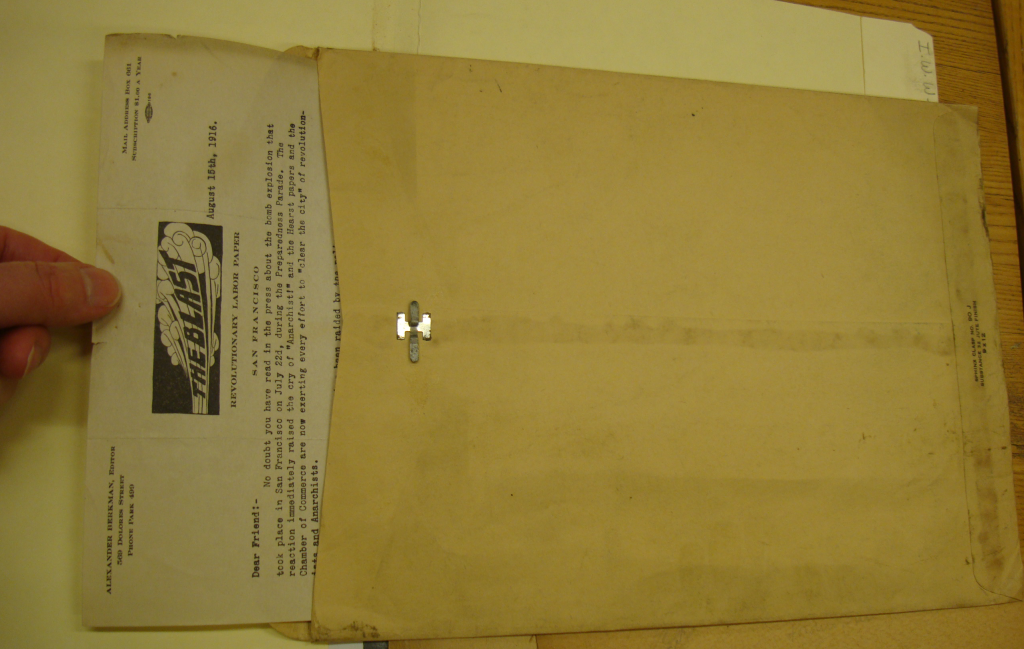 Fig 3b. Color photo of the same brown envelope. A hand drawing the letter out. Letter has text image stating “The Blast” and typewriter written text.