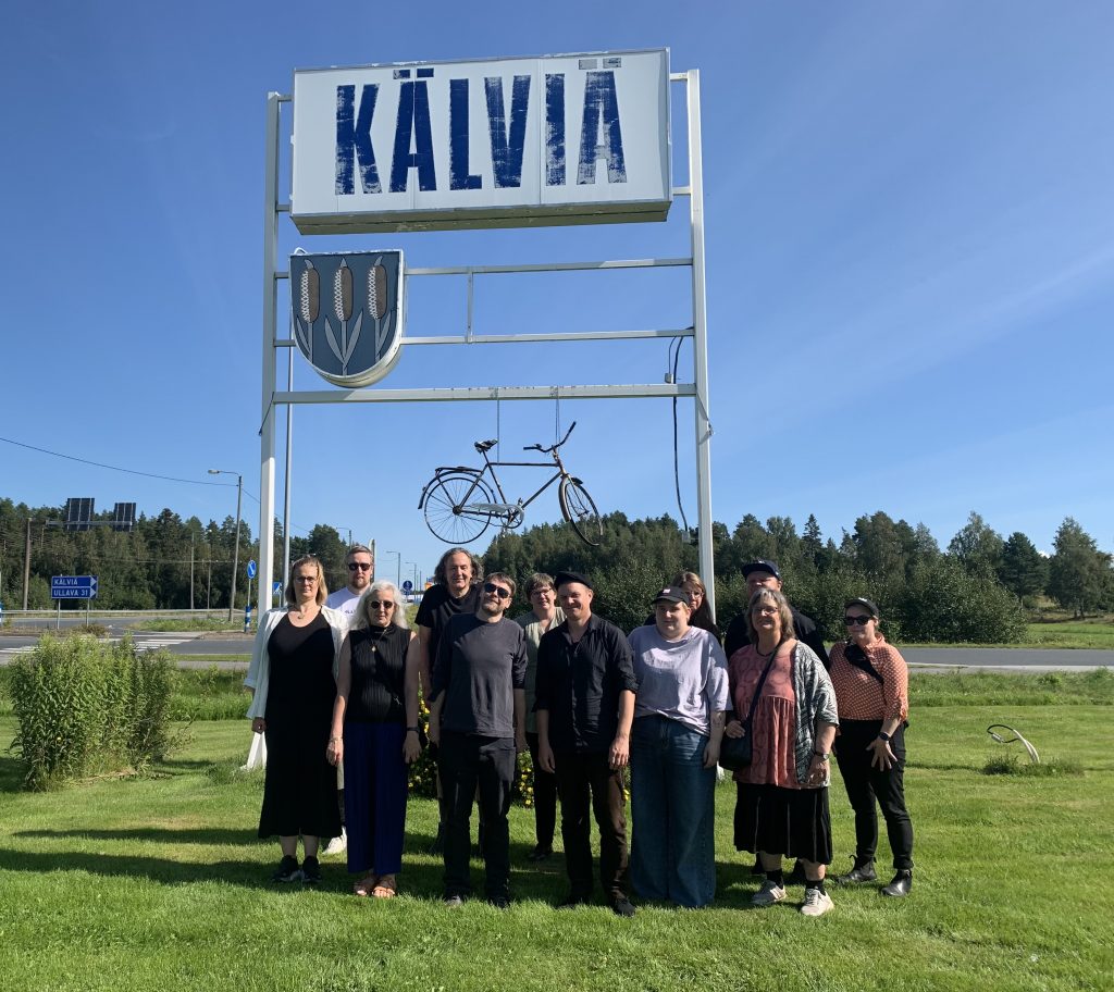 Group of people standing on grass field, under sign that says "KÄLVIÄ".