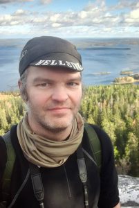 Picture of Tuomas Tammisto on cliff and in the background a lake and forest in Finland.